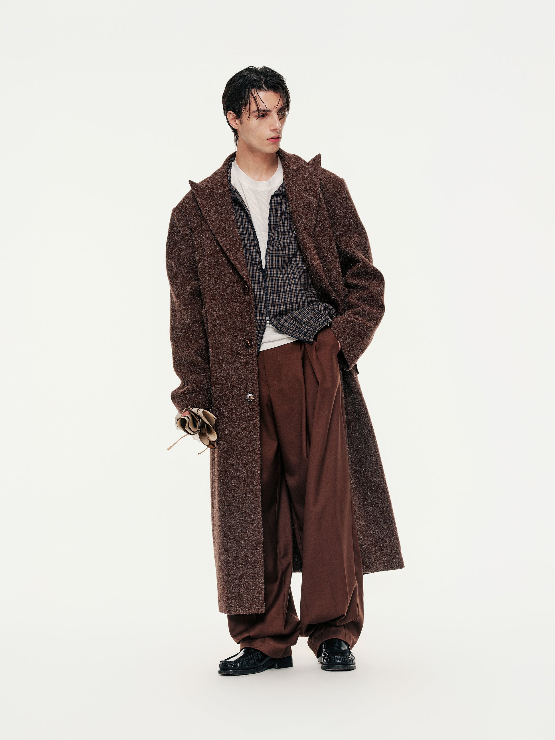 Person wearing a long brown coat and pants on a white background