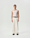 Person wearing a light pink sleeveless top and white pants on a plain background