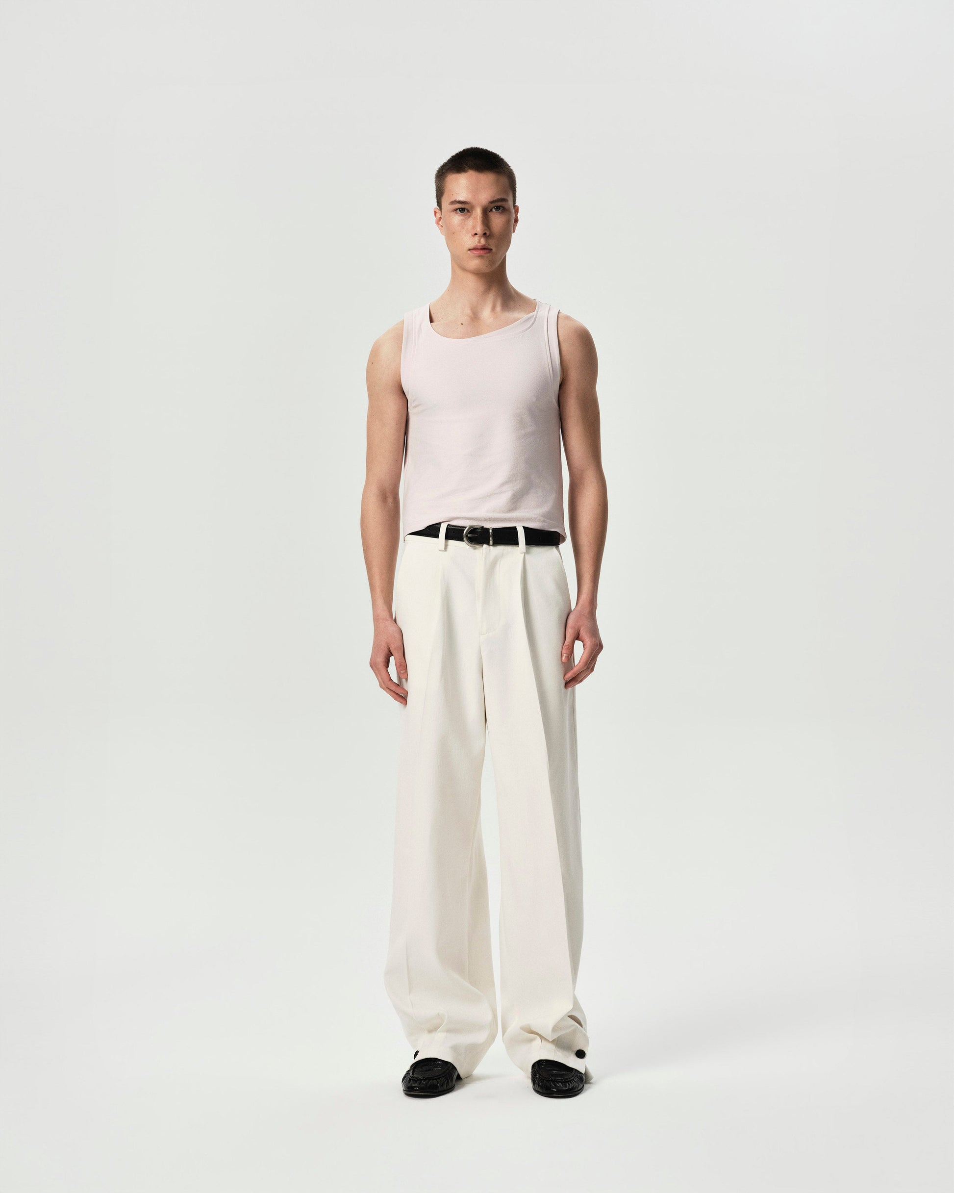 Person wearing a light pink sleeveless top and white pants on a plain background
